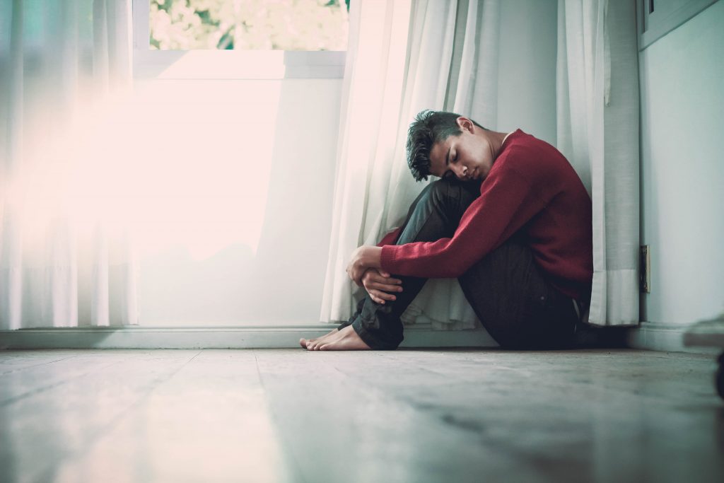 Teen sitting clutching knees in a corner with eyes closed