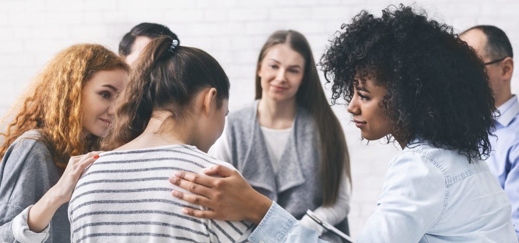 Group of women and men sitting in a circle with one woman being comforted by people beside her