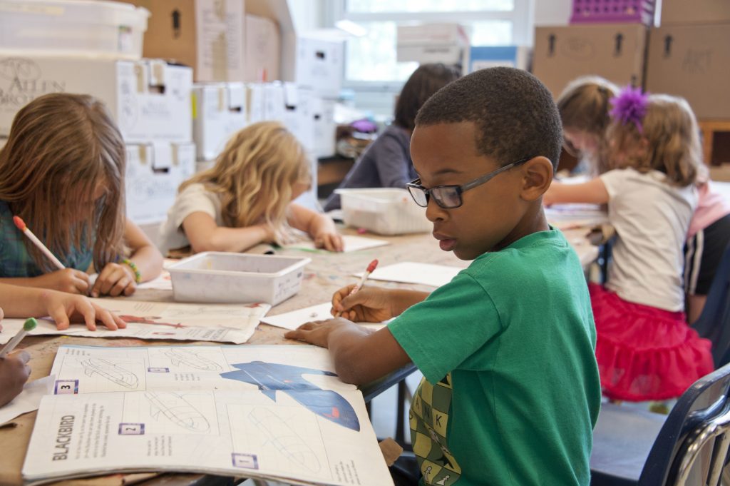 Young children working on a workbook project at a large table in a school classroom.