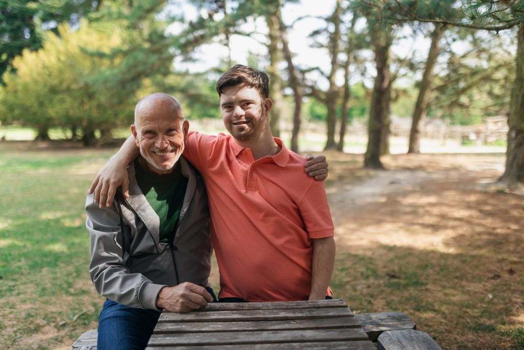 An adult with down syndrome hugging another adult to his left side.