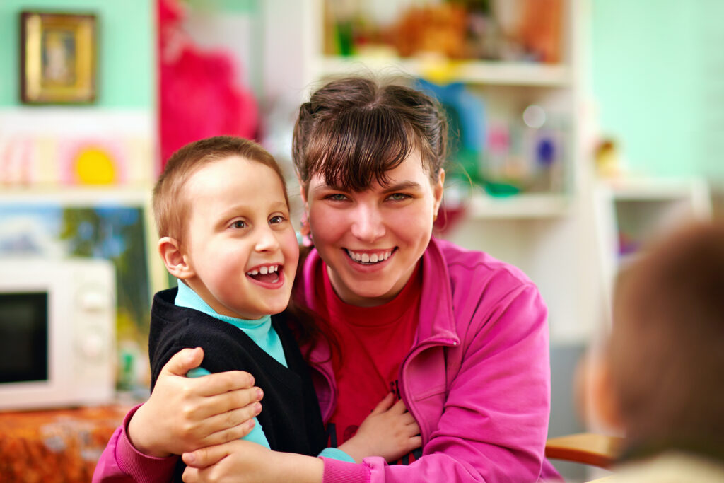 Two individuals with disabilities hugging each other in a classroom.